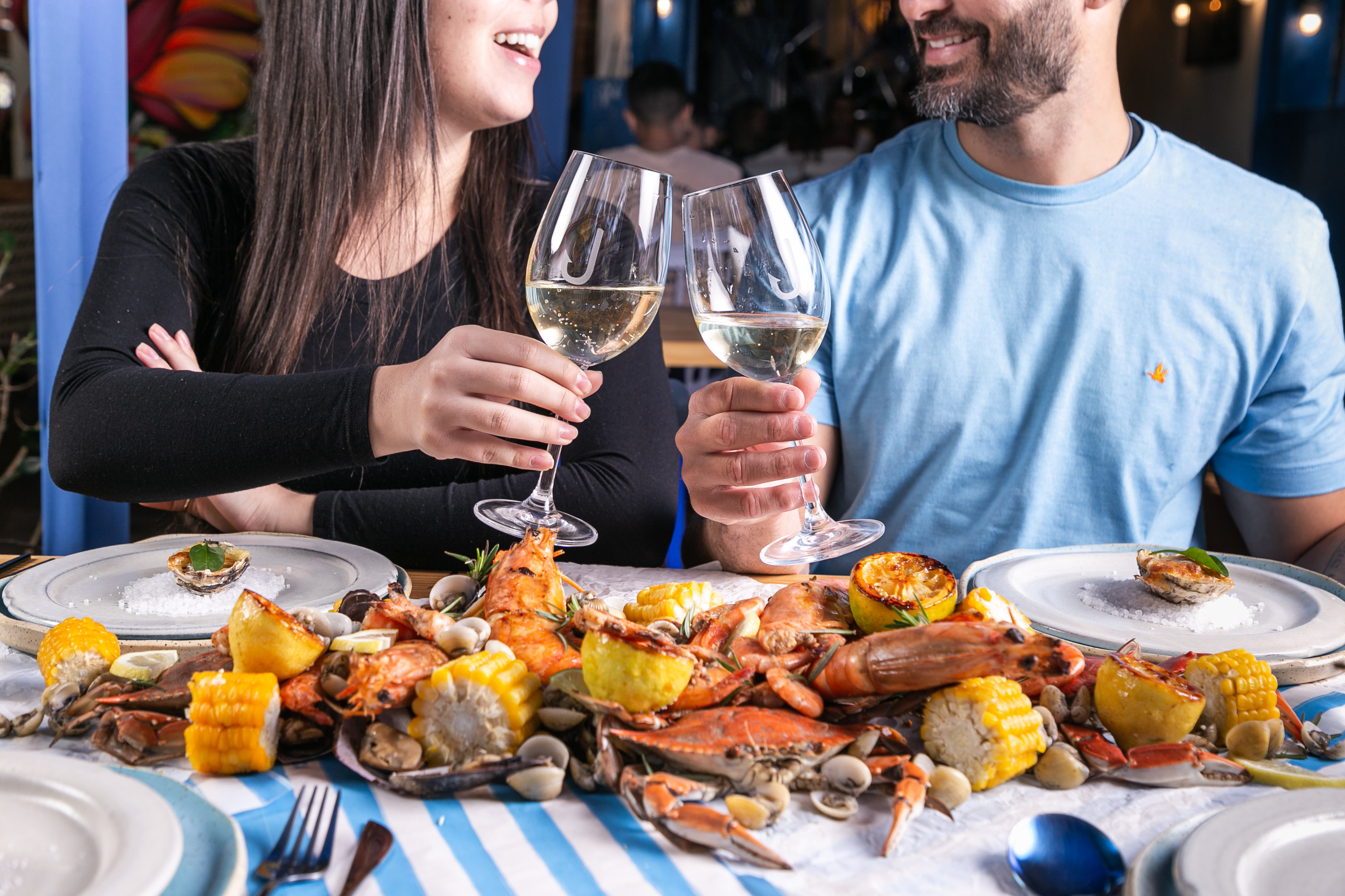 Mesa posta com frutos do mar, limões, milho e mariscos, em toalha listrada azul e branca