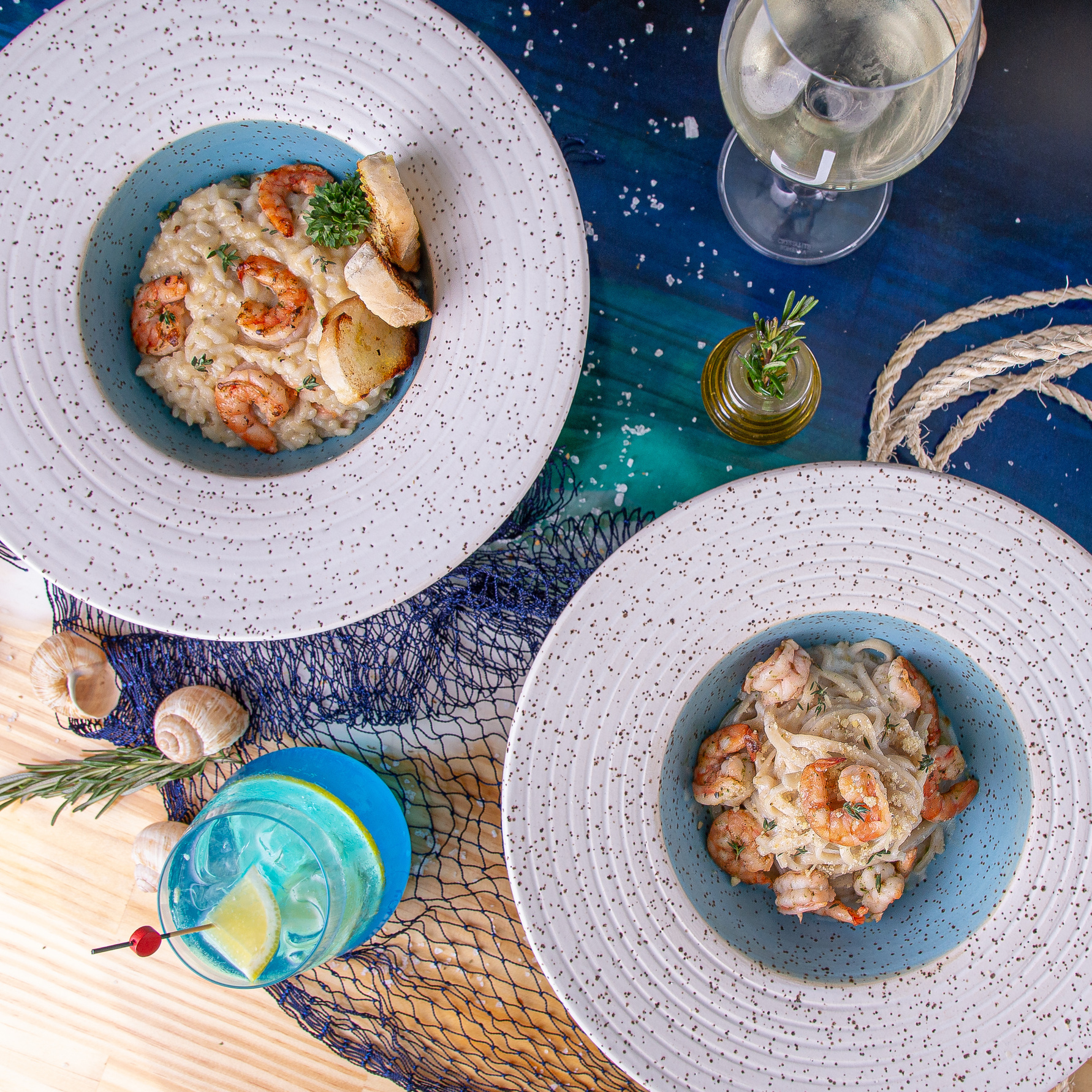 Risoto cremoso com camarões e torradas, em prato azul sobre tecido de rede de pesca