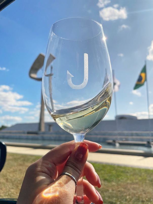 Taça de vinho branco com o J da marca gravado, em frente a um céu azul